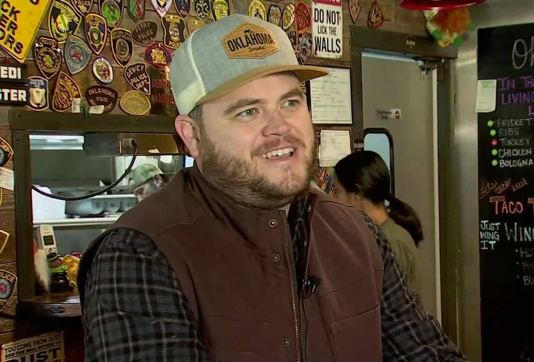 Owner Ean Kampmeyer in an Oklahoma Smoke cap, in front of the wall of police and fire department patches